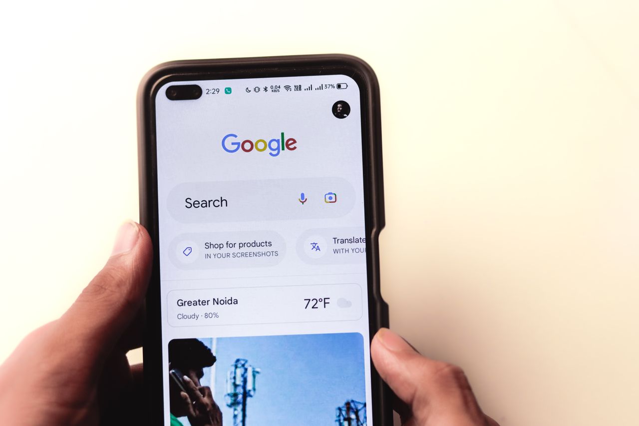 Vue rapprochée d’une main tenant un smartphone avec la recherche Google affichée à l’écran.